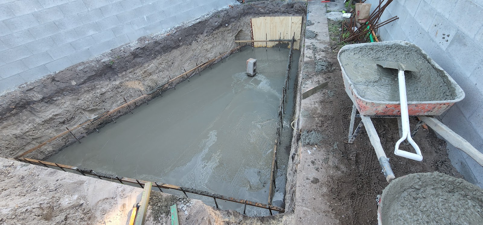 Freshly poured concrete in a formed trench beside a wheelbarrow on a job site