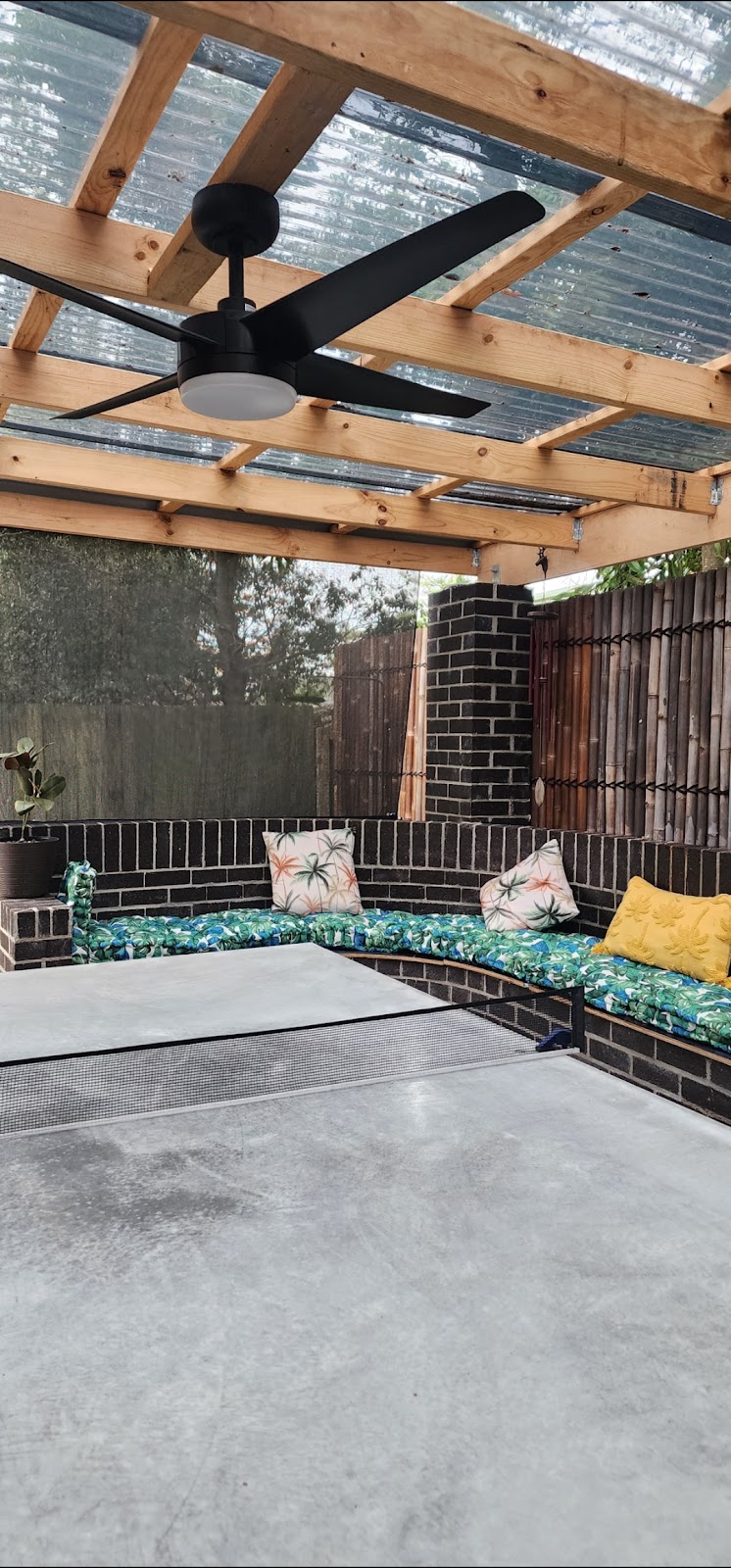 Dark brick built-in U-shaped bench seating with cushions under a pergola